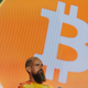 Jack Dorsey staring off to the right in front of a giant bitcoin symbol on a large screen.